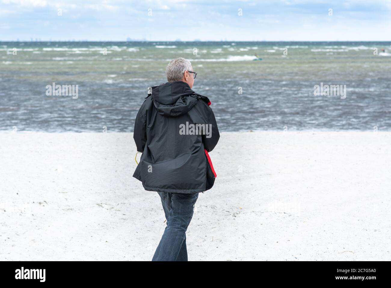 A middle-aged man, 50 plus, walks along a white beach. Outdoor activities that include social distance is safe activities during the coronavirus pandemic. Blue sky, turquoise water in the background Stock Photo