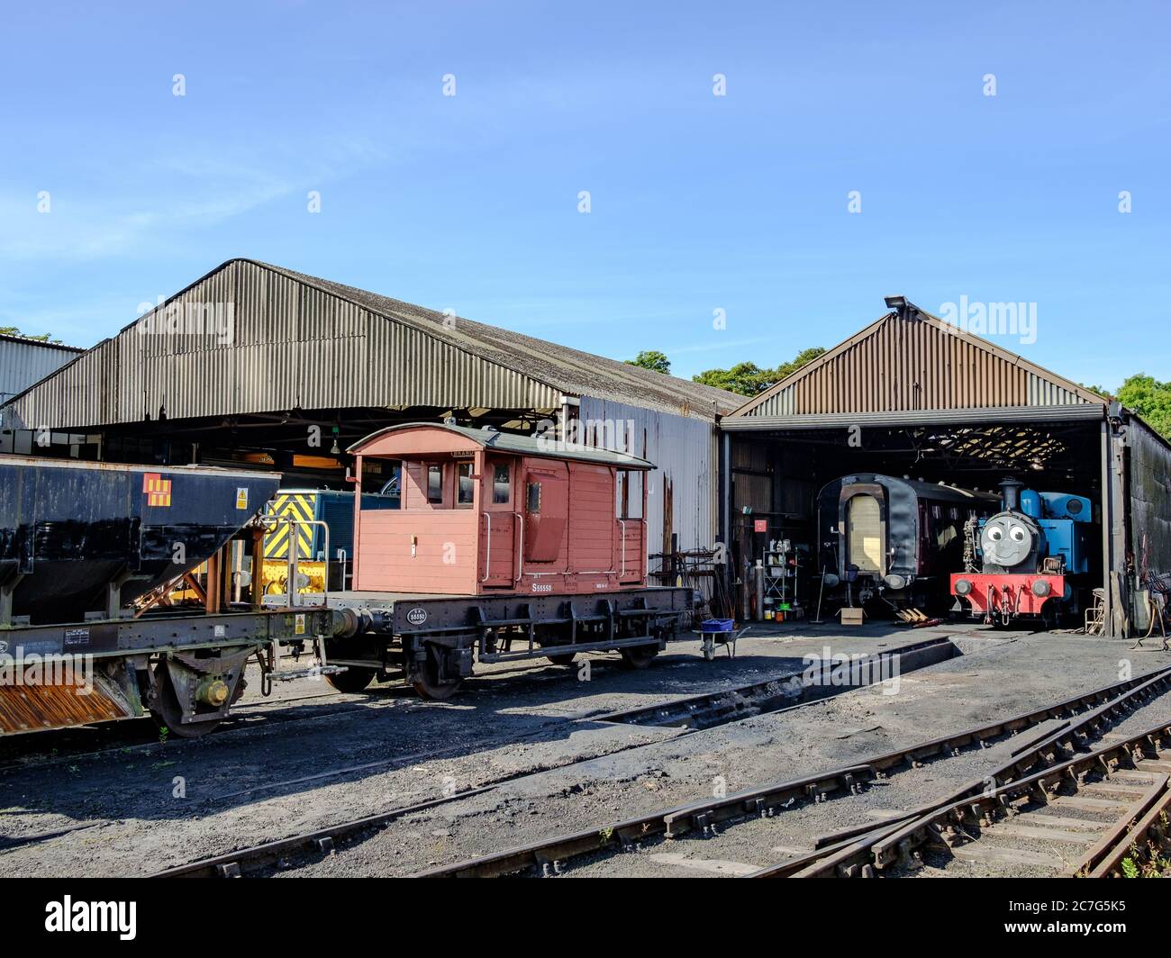 Vintage styled steam locomotives including a popular children's character train seen in a locomotive shed with a train driver seen walking past. Stock Photo