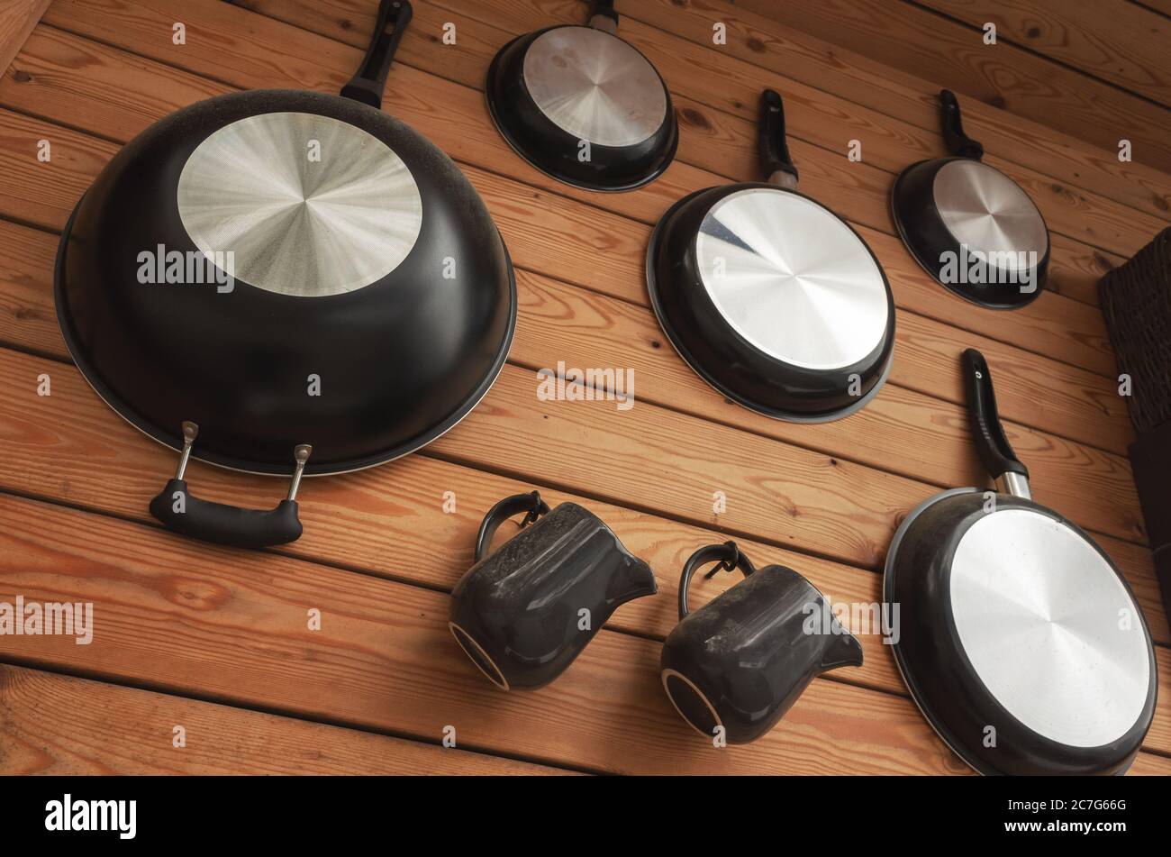 Black frying pans are hanging on wooden wall Stock Photo