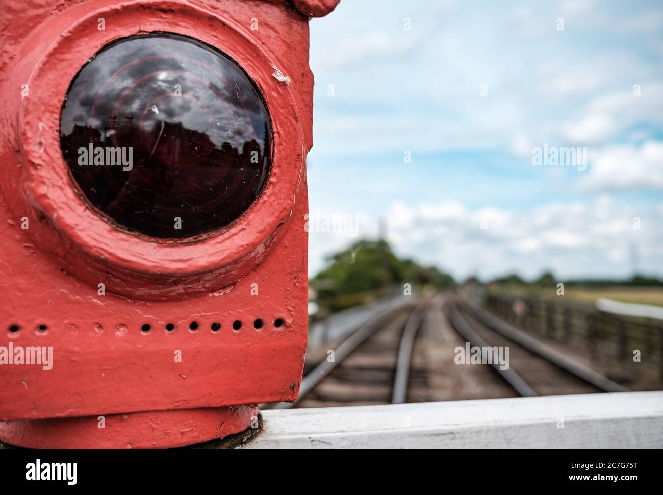 Close-up view of a vintage stop lantern seen atop an old railway level crossing, with distant out of focus railway tracks curving to the distance. Stock Photo