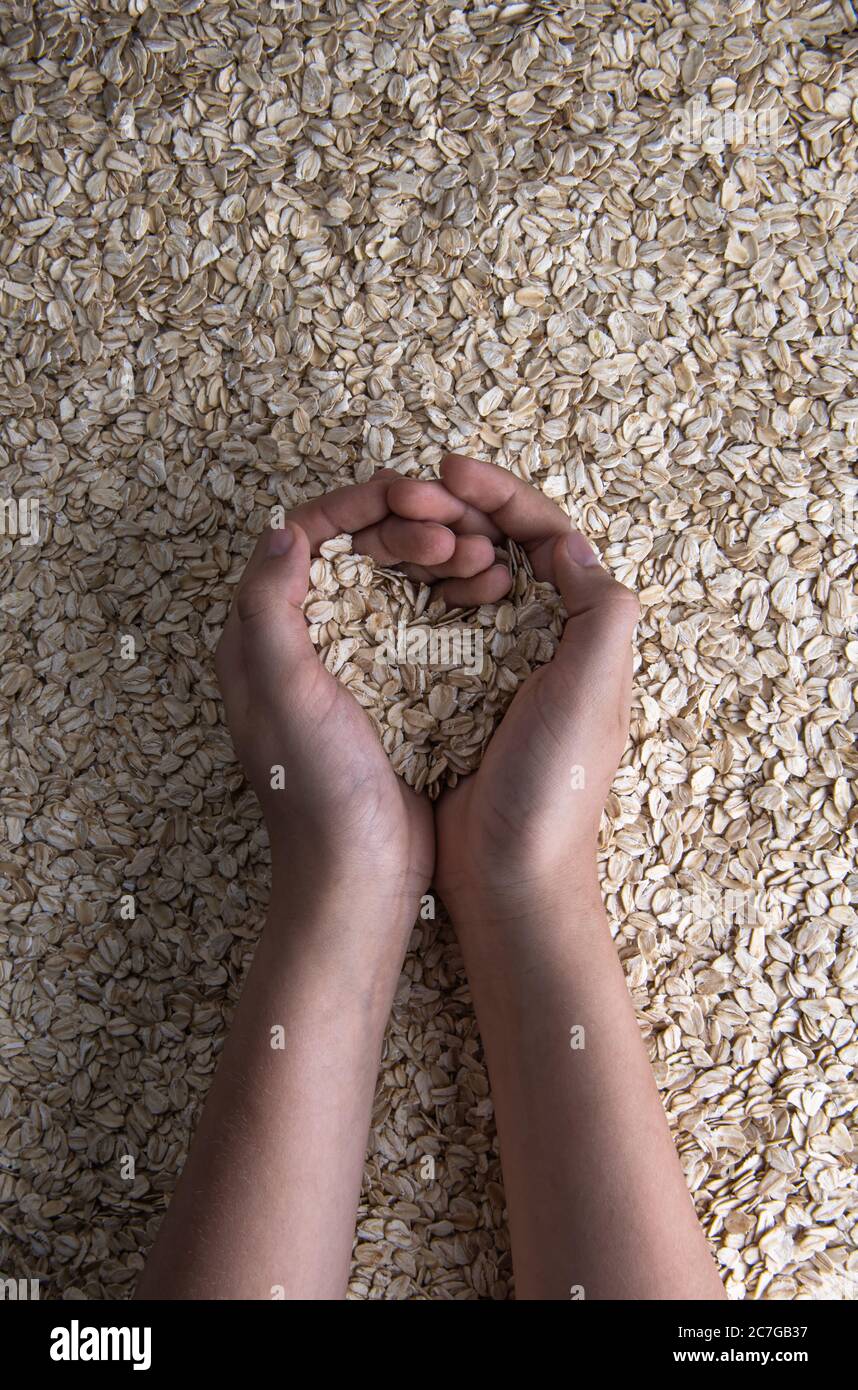 Cupped teenager hands with rolled oats in shape of heart. There is some natural oat flour on fingers. Raw rolled oats background. Healthy and sport ea Stock Photo