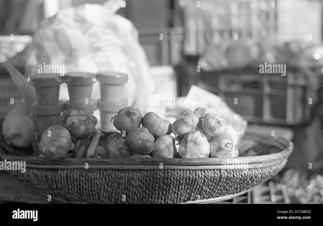 Grey scale shot of a basket full of garlic with some buildings in the background Stock Photo