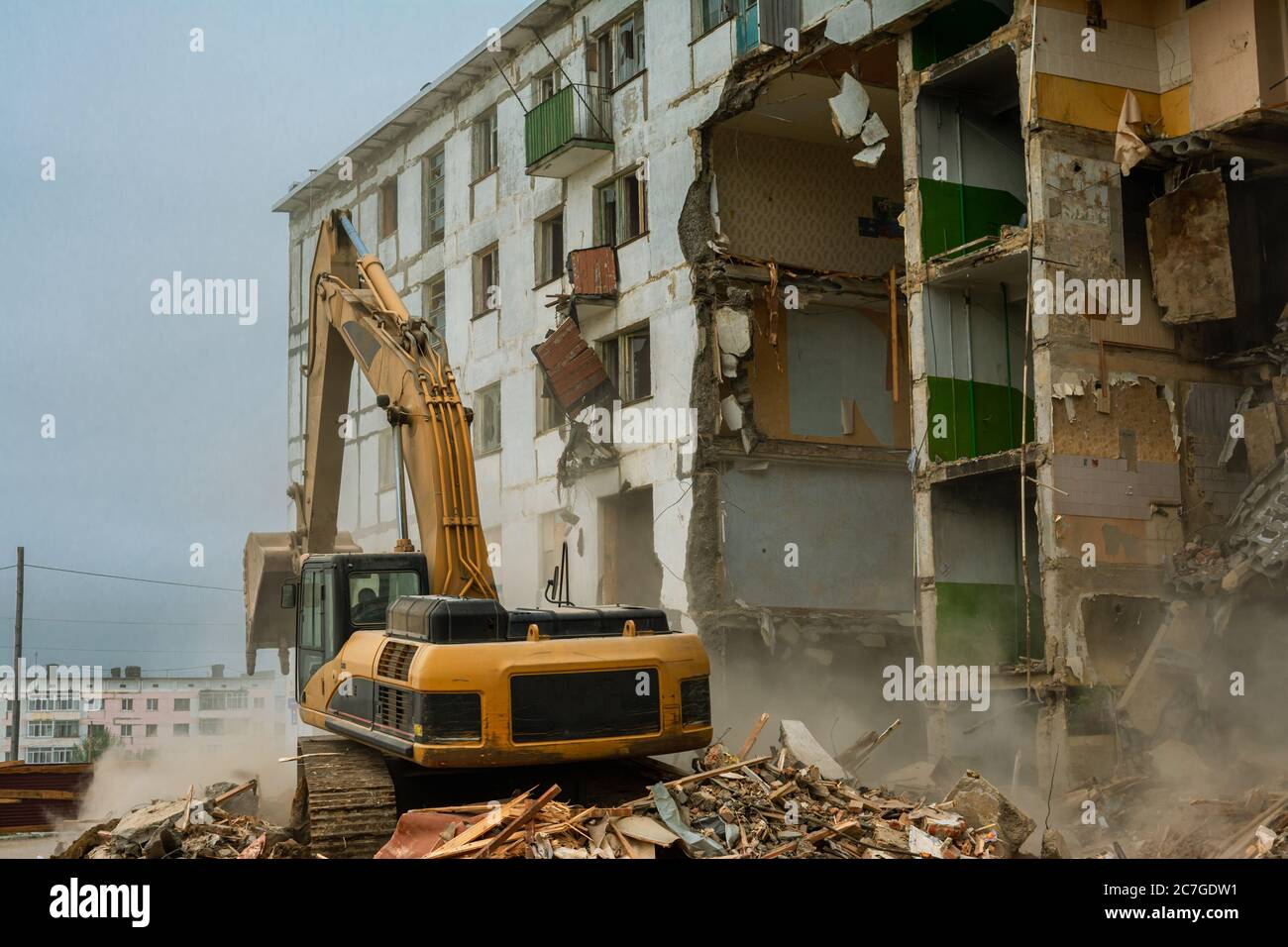 Demolition of a five-story apartment building recognized as emergency housing, close-up of an excavator bucket collects construction waste Stock Photo