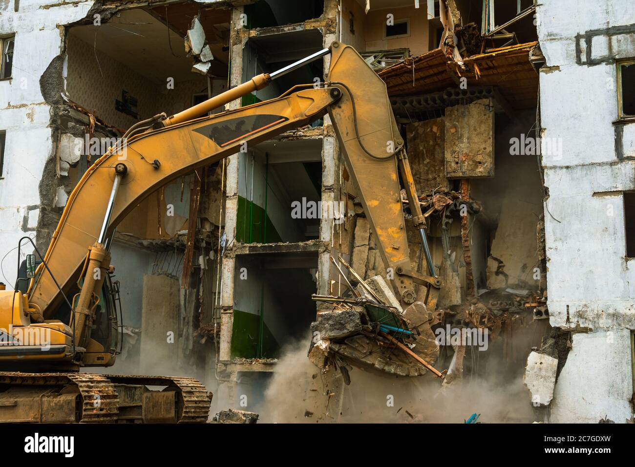 Demolition of a five-story apartment building recognized as emergency housing, close-up of an excavator bucket collects construction waste Stock Photo