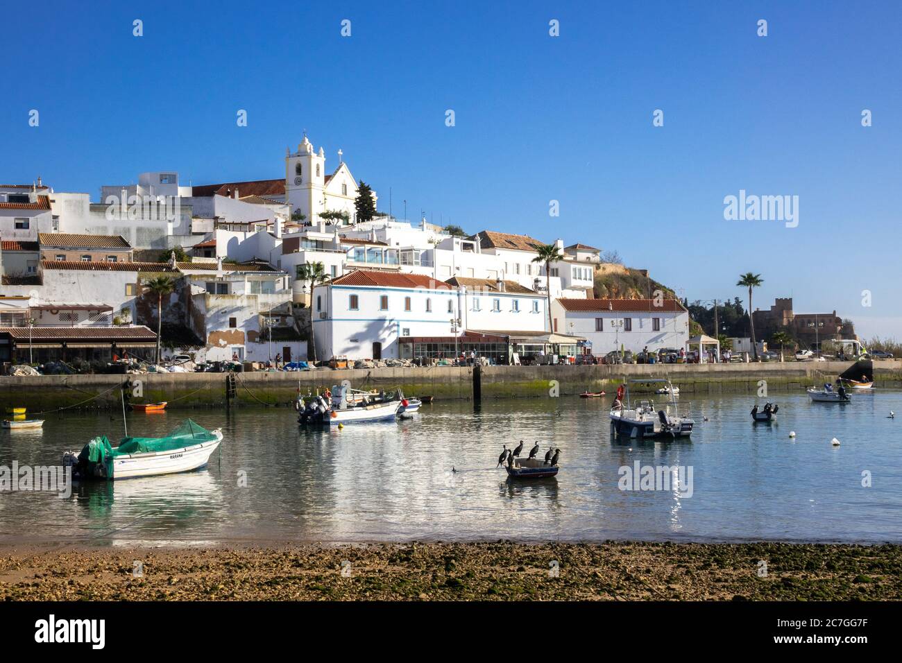 The Town Of Ferragudo From Across The Arade River Estuary The Algarve Portugal On The Hill The Church of Nossa Senhora da Conceição Stock Photo