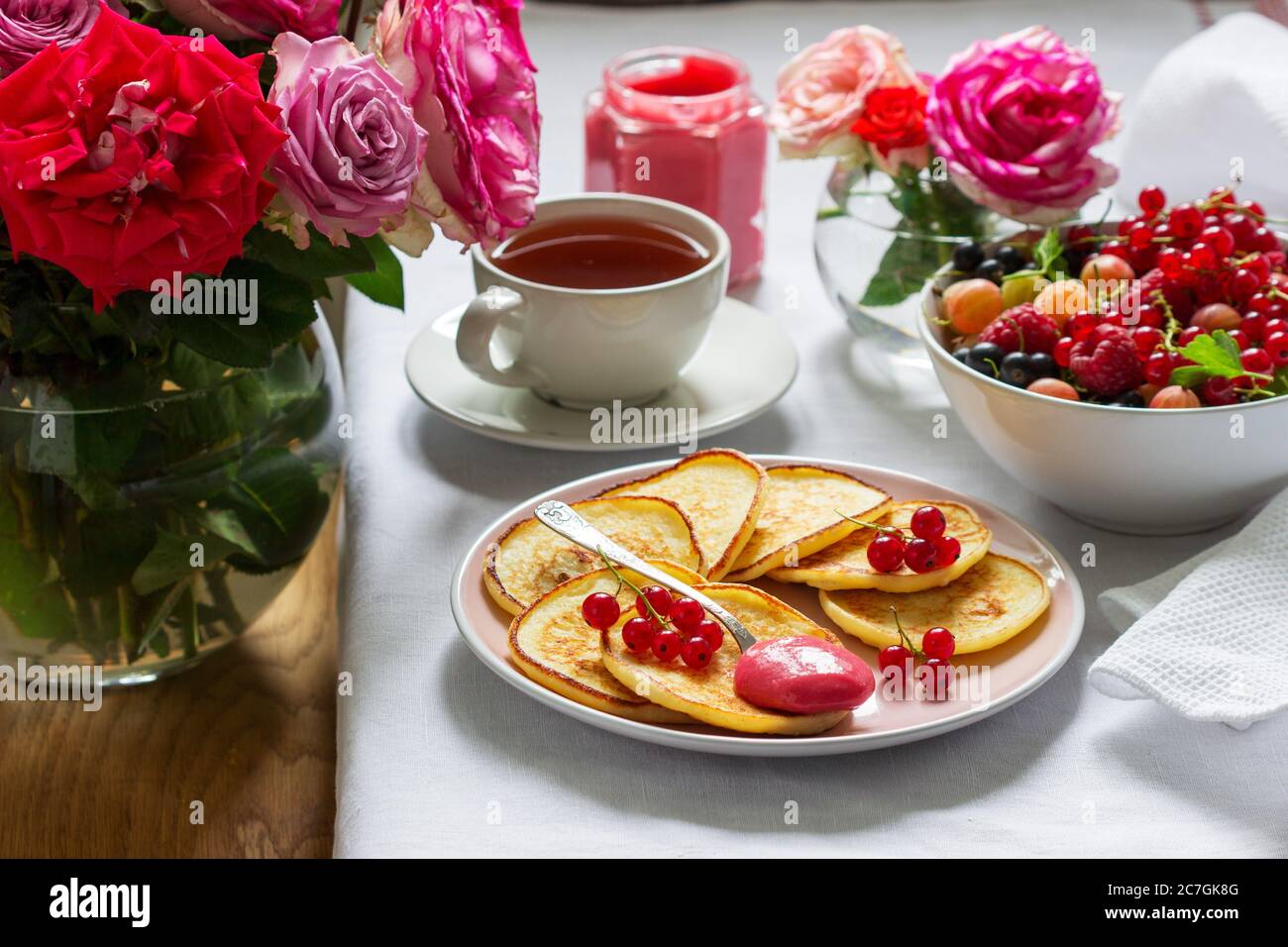 Curd pancakes with berry curd served with tea on a table decorated with bouquets of roses. Stock Photo