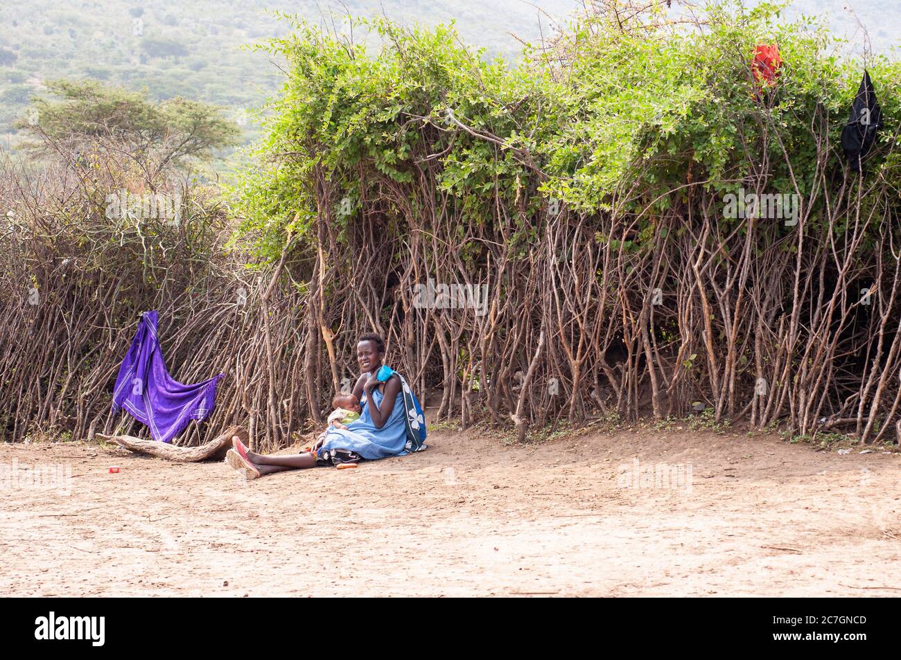 Maasai young mother and baby, wearing traditional attire sitting on the floor, in a maasai village, in Maasai Mara National Reserve. Kenya. Africa. Stock Photo