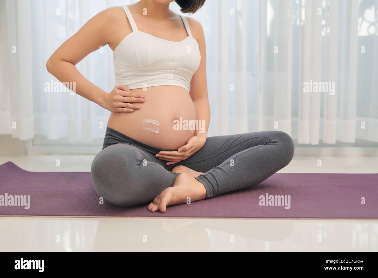 pregnancy, people and maternity concept - happy pregnant asian woman applying stretch mark cream to belly Stock Photo