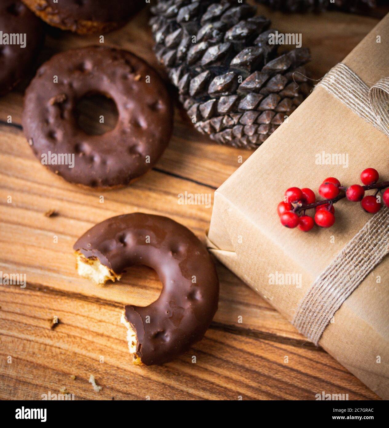 High angle closeup shot of a half-eaten chocolate doughnut next to a wrapped gift and a pine cone Stock Photo
