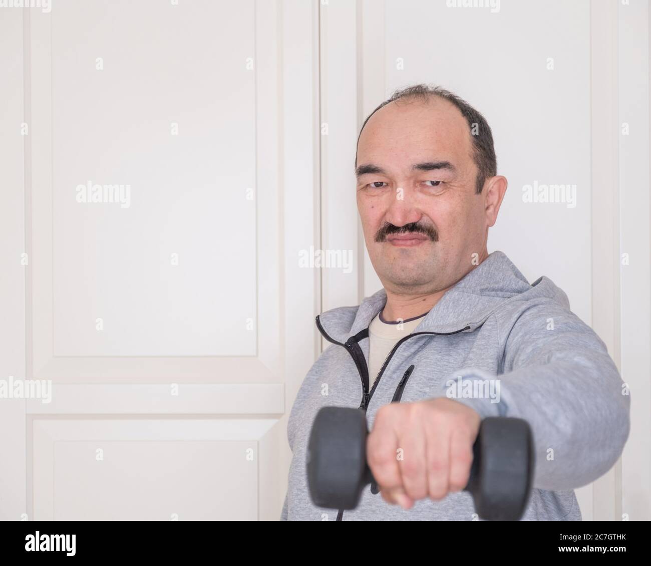 Asian senior athlete in sweatshirt doing fitness at home with sports equipment. Copy space Stock Photo