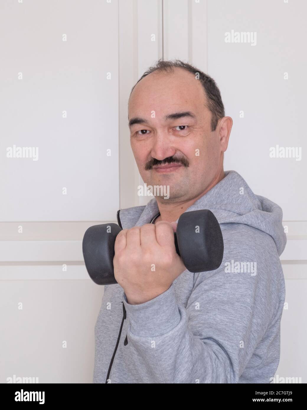 Asian man in activewear doing fitness at home with sports equipment. Stock Photo