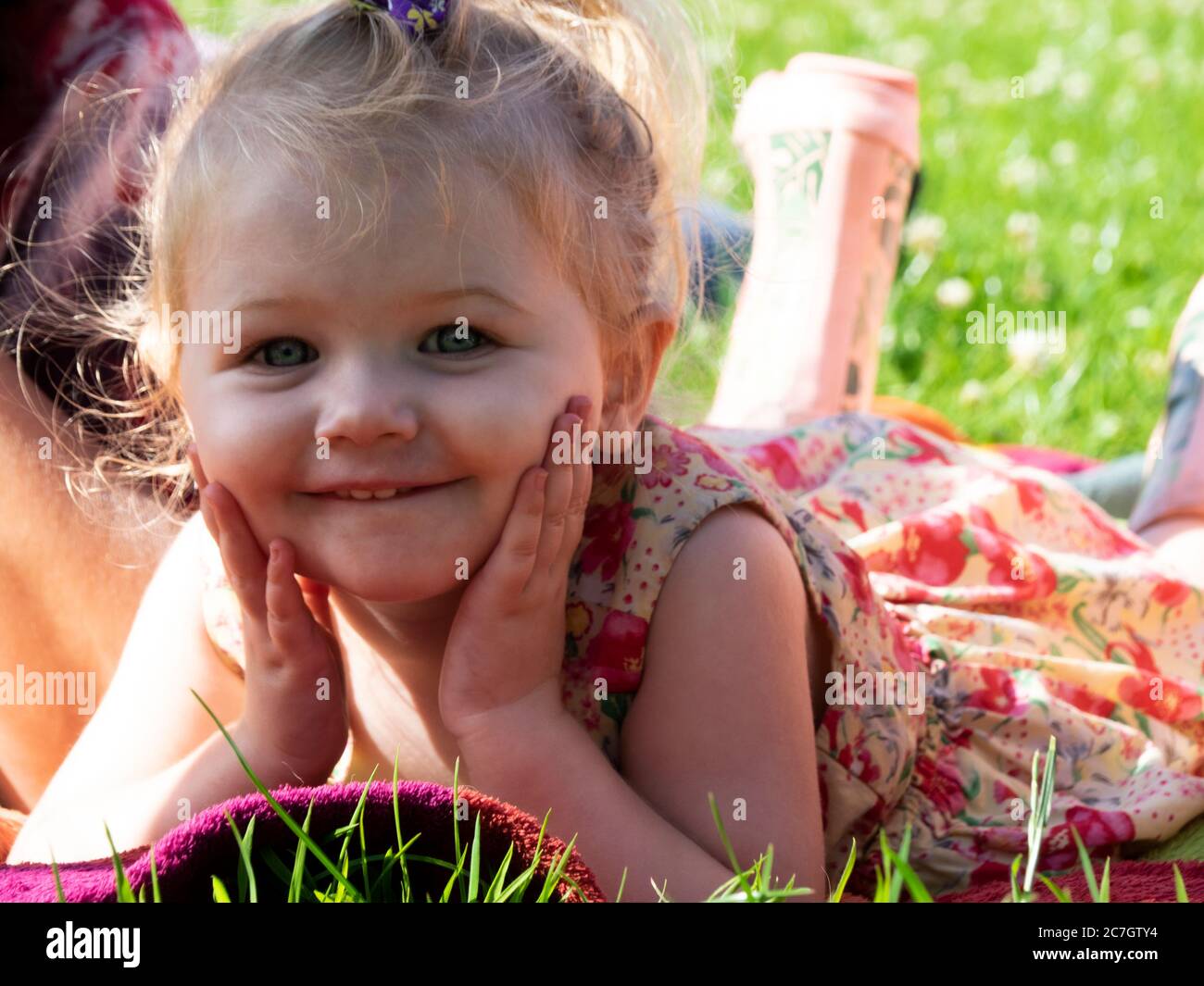 Toddler lying on a blanket with hands under chin, UK Stock Photo