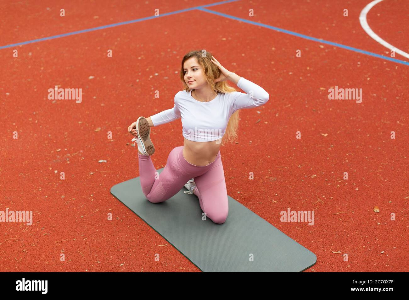 Yoga, pilates, fitness concept. Pretty young woman in pink sport suit, practicing yoga Eka Pada Rajakapotasana Pose, on the fit mat at the red coated Stock Photo