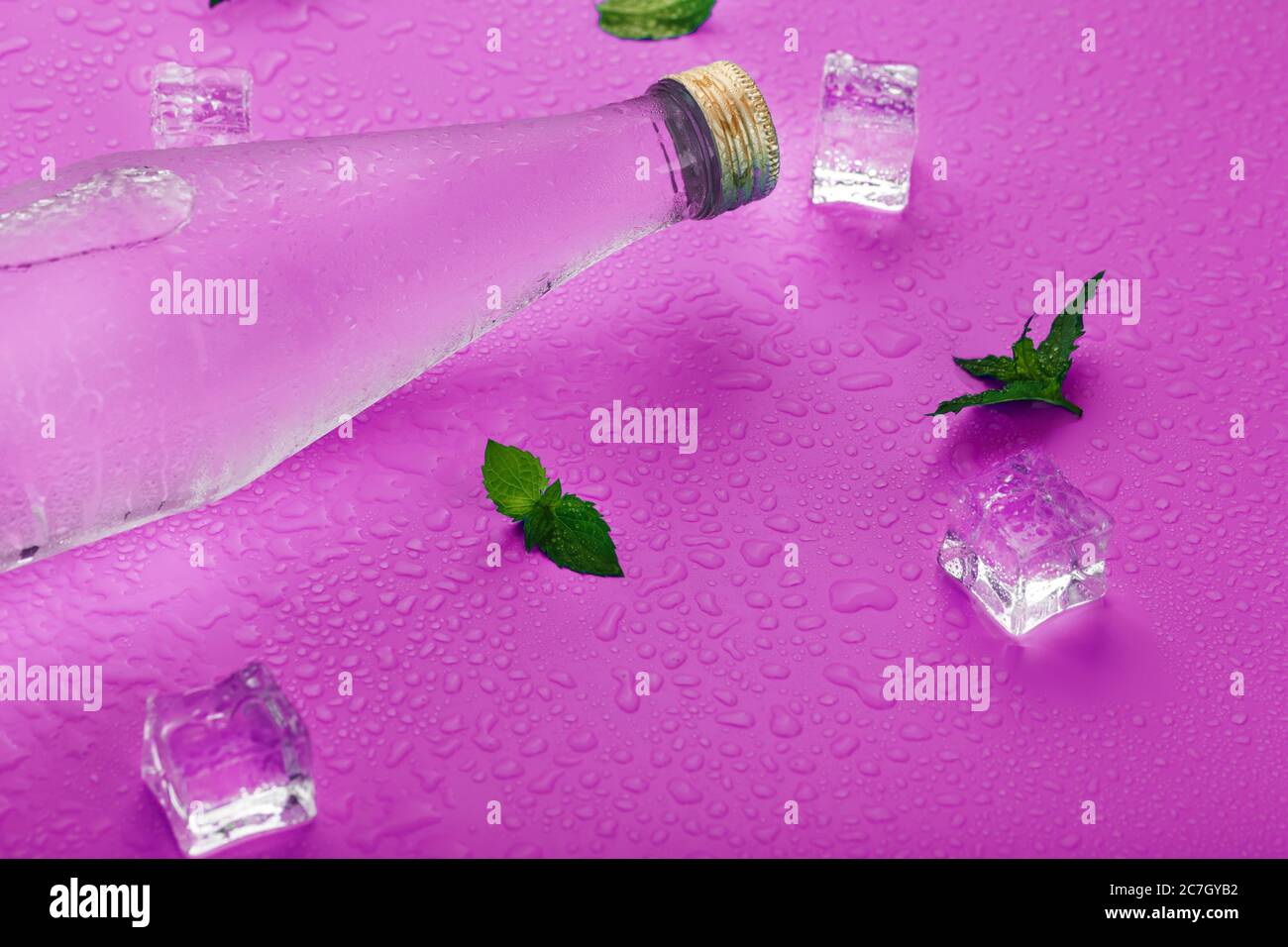 Bottle with an ice cold beverage, ice cubes, drops and mint leaves