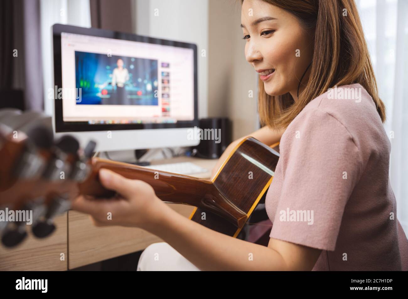 Asian woman guitar player and vlogger playing guitar in the front computer at home while social distancing of coronavirus outbreak Stock Photo