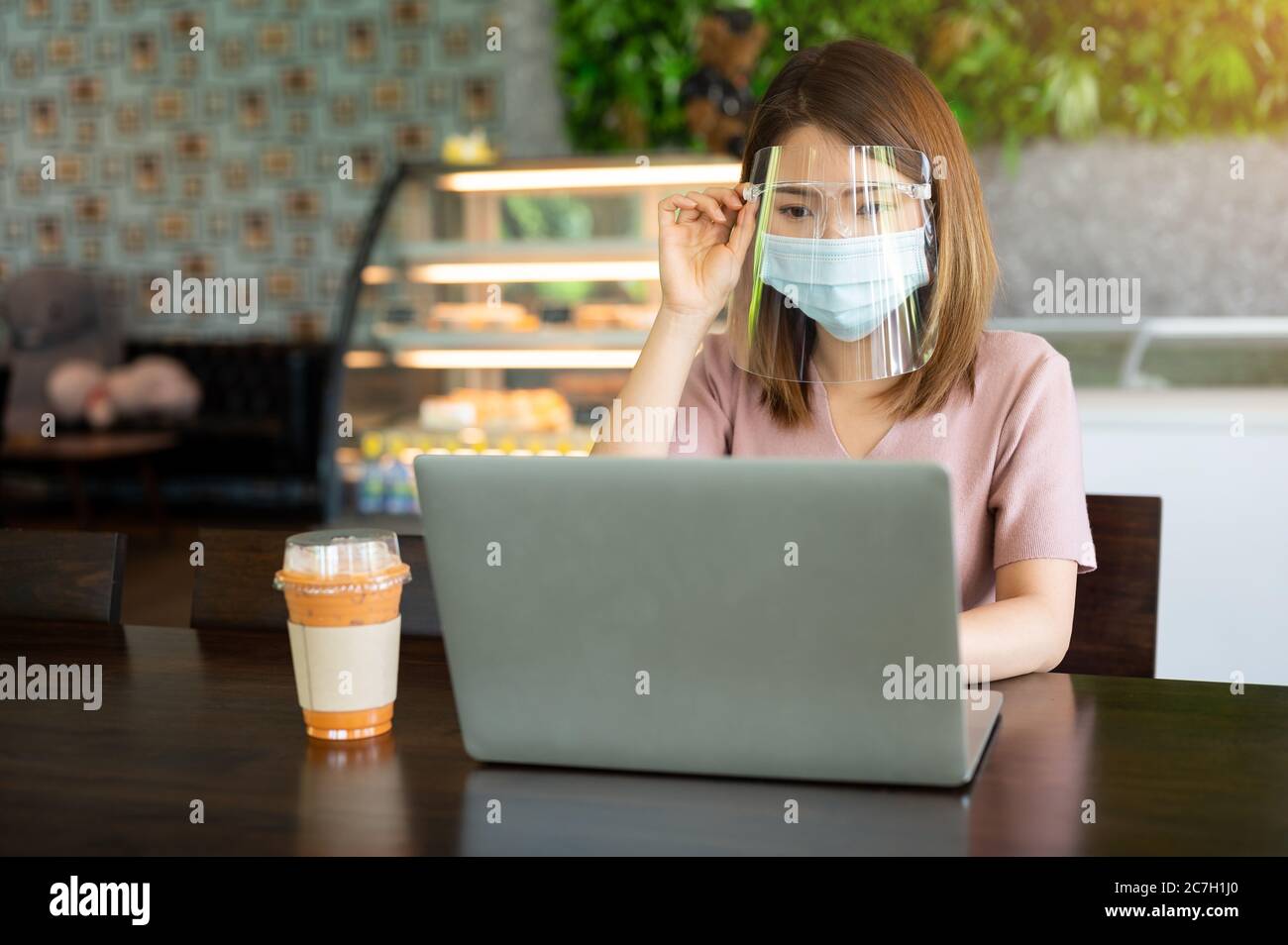 Asian woman wearing face shield and protective mask working on laptop ...