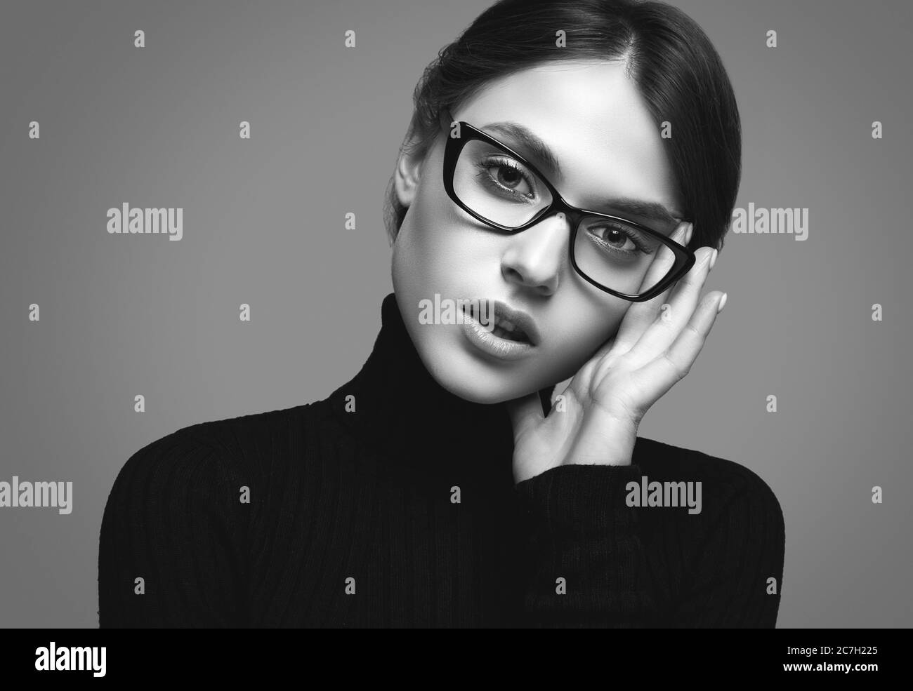 Portrait of cute student girl wearing black turtleneck sweater and stylish eyeglasses posing on gray background in studio Stock Photo