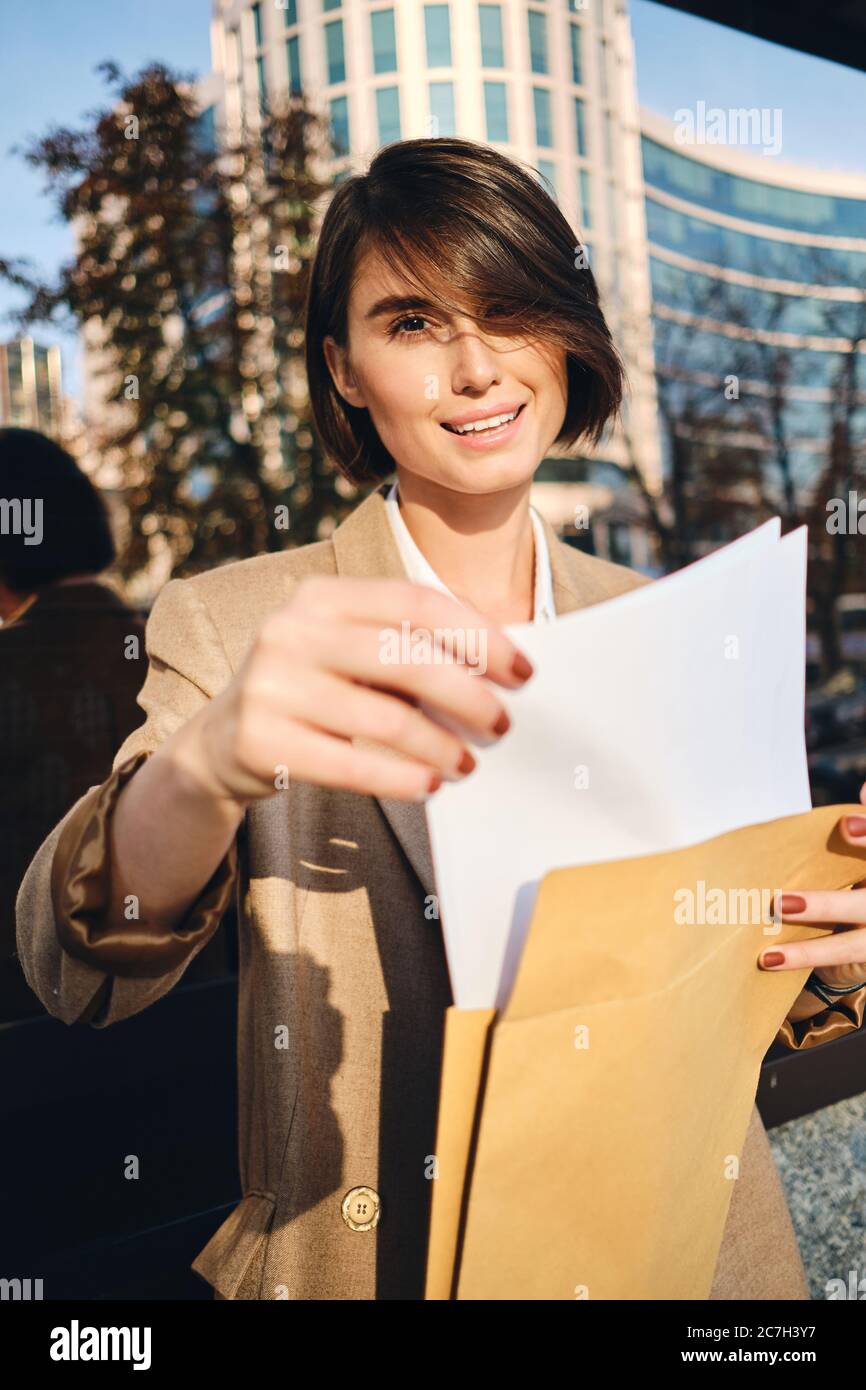 Young attractive stylish businesswoman opening envelope happily looking in camera on city street Stock Photo