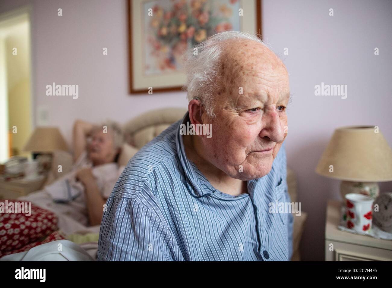 Elderly couple in their 80's sat on the bed in their pyjamas before getting up in the in the morning, England, United Kingdom Stock Photo