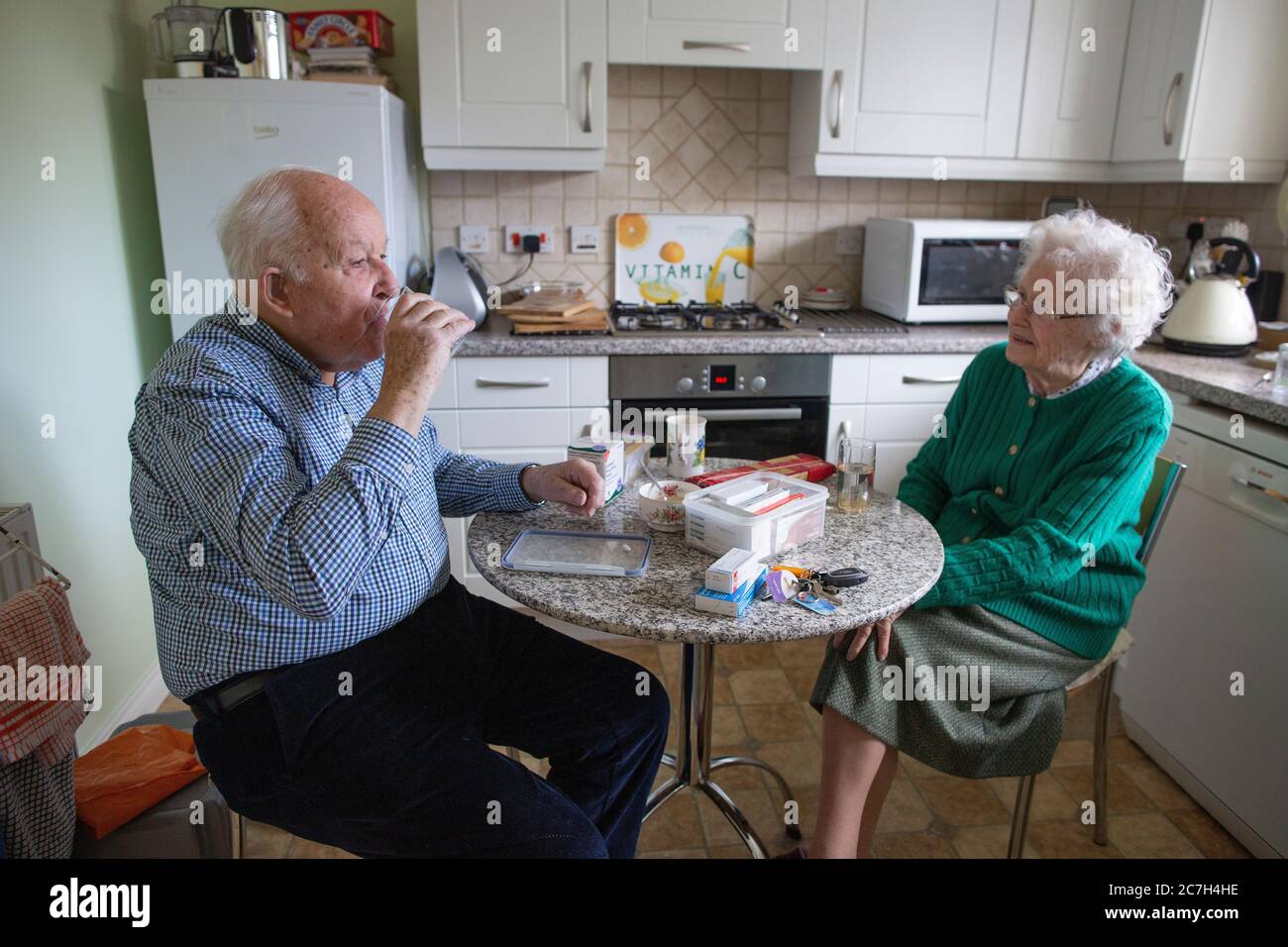 Elderly couple in their 80's taking medication whilst sat at the breakfast table drinking a cup of tea in the morning, England, United Kingdom Stock Photo