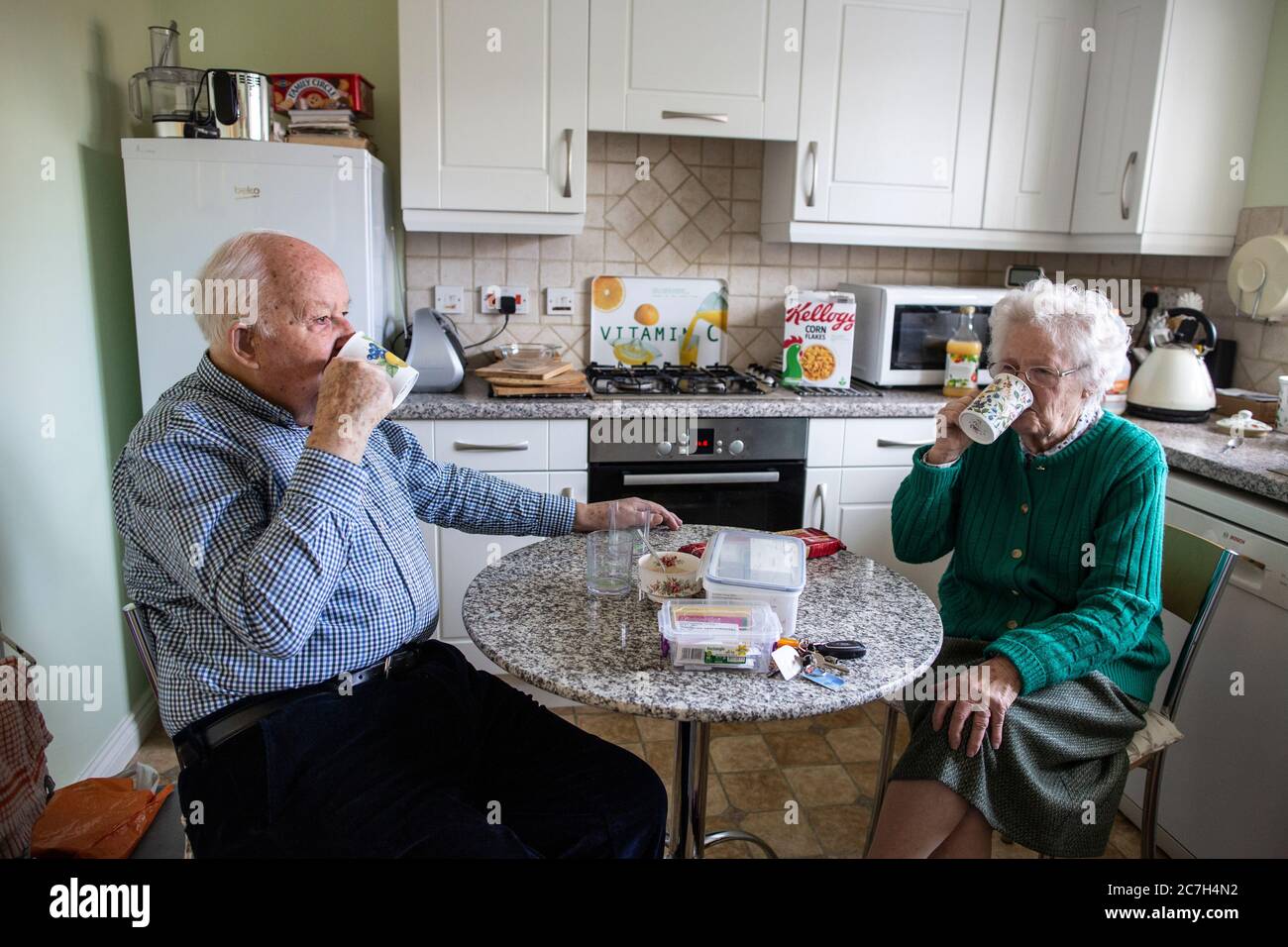 Elderly couple in their 80's taking medication whilst sat at the breakfast table drinking a cup of tea in the morning, England, United Kingdom Stock Photo