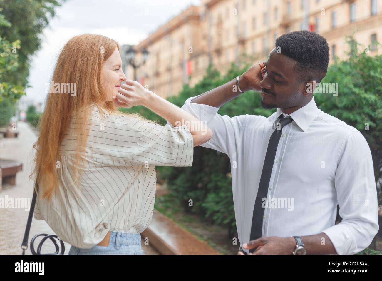 Elbow bump greeting to avoid the spread of coronavirus. Black man and caucasian woman use elbows instead palms for greeting Stock Photo