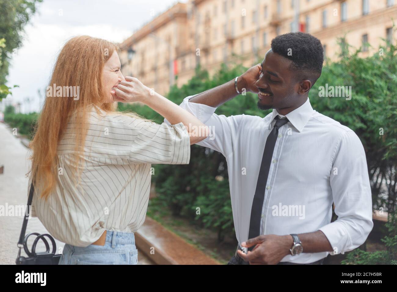 Elbow bump greeting to avoid the spread of coronavirus. Black man and caucasian woman use elbows instead palms for greeting Stock Photo