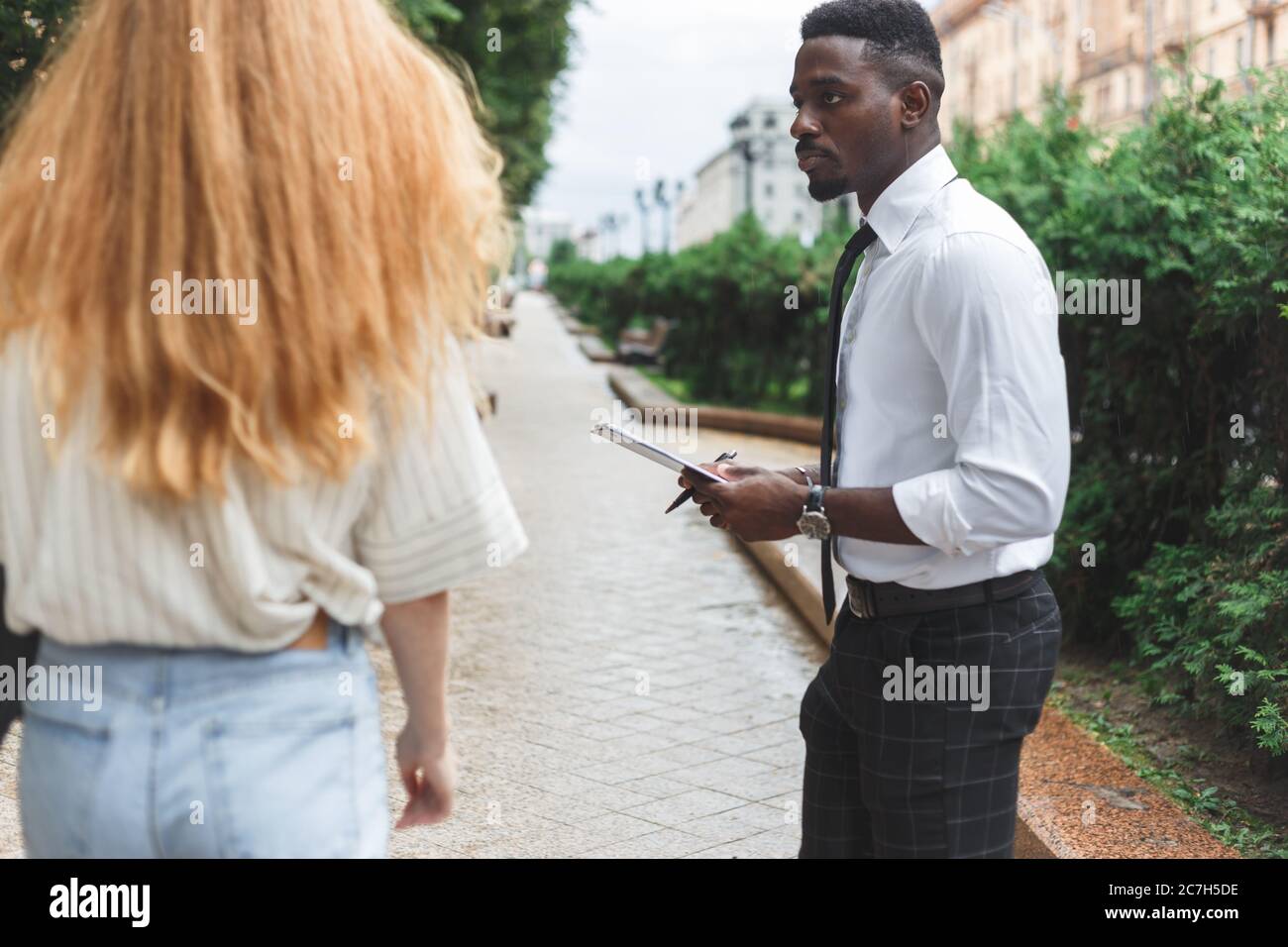 Obsessive black man in business attire interview on the street bothering passersby with questions Stock Photo