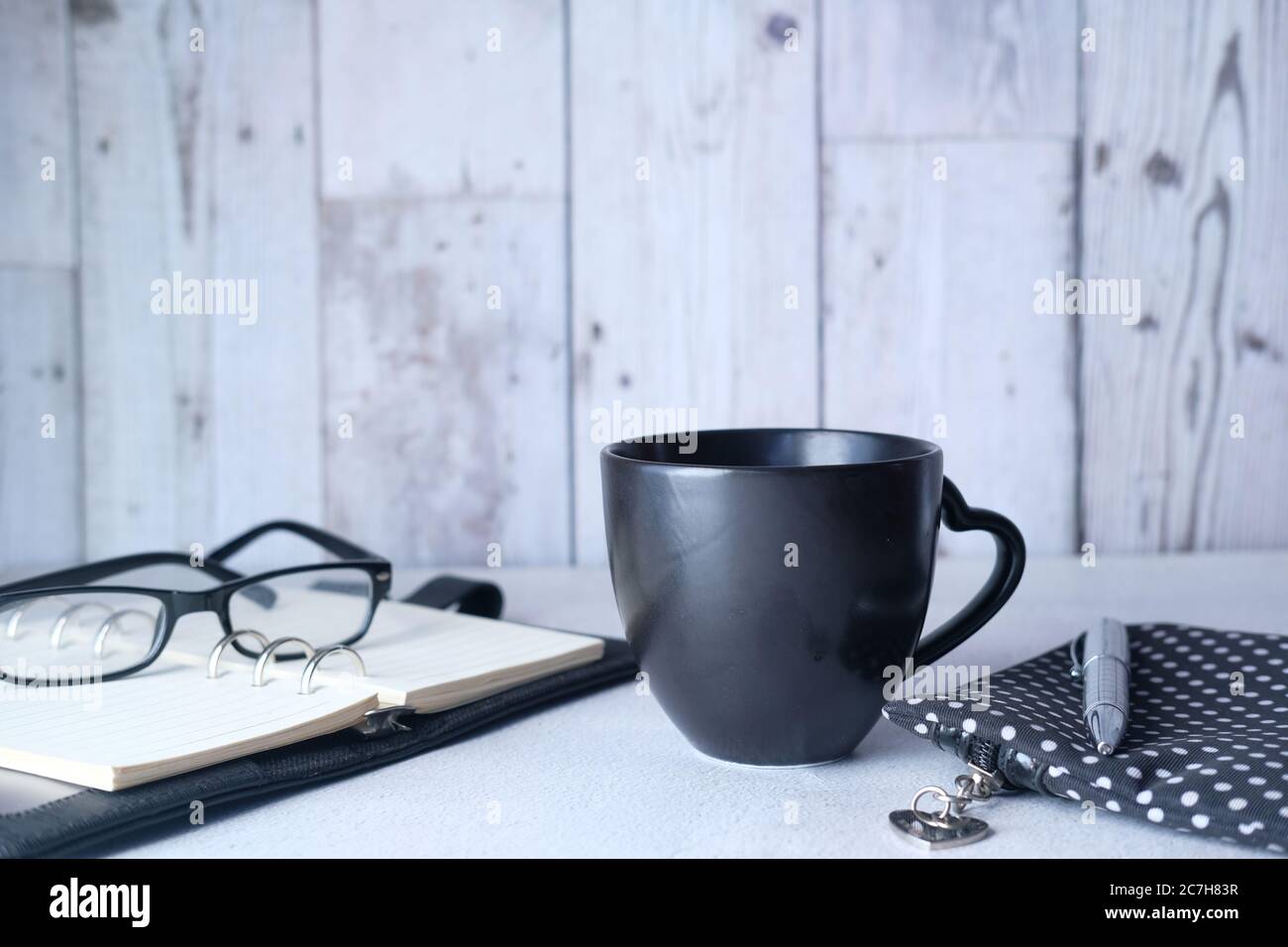 black mug mockup, modern workspace with notepad and eyeglass on table. Stock Photo