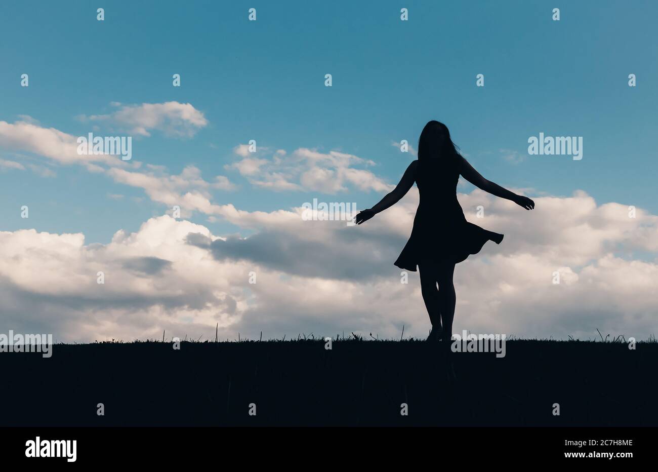 Silhouette of woman in a dress dancing against a blue sky with clouds. Stock Photo