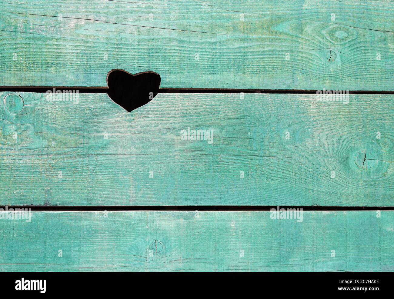a hole in the shape of a heart in a wooden wall made of old boards painted blue Stock Photo