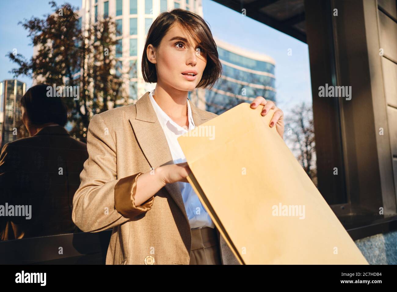 Young attractive stylish businesswoman excitedly opening envelope working with papers on city street Stock Photo