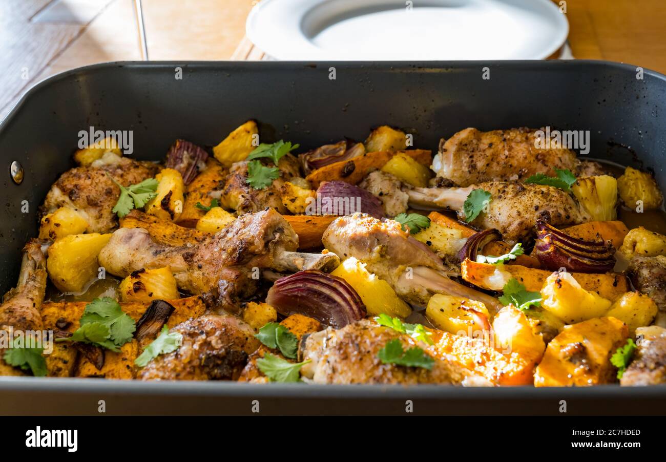 Jerk chicken drumsticks & thighs tray bake in roasting tin with vegetables: sweet potatoes, red onions & pineapple chunks Stock Photo