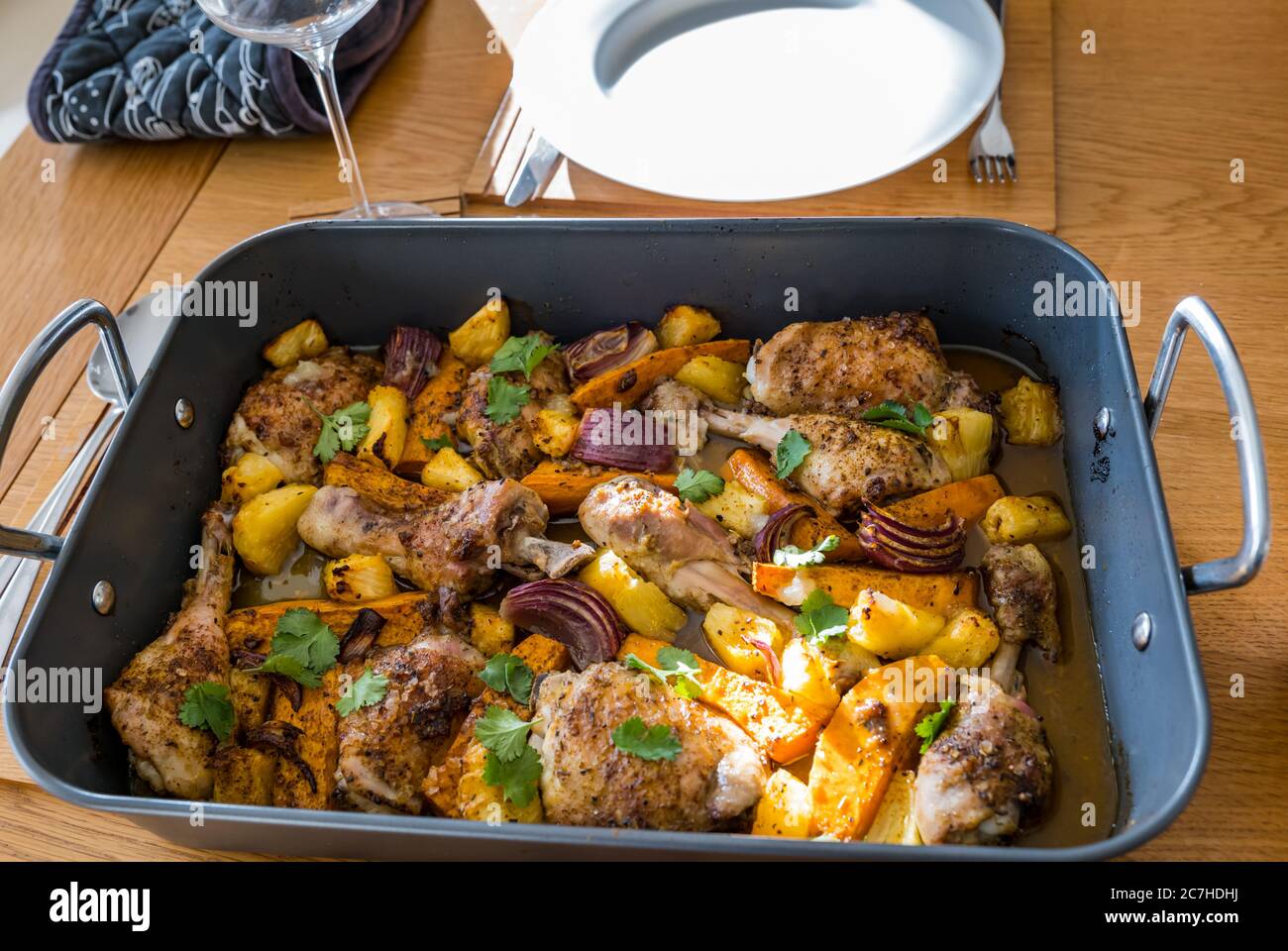 Jerk chicken drumsticks & thighs tray bake in roasting tin with vegetables: sweet potatoes, red onions & pineapple chunks Stock Photo