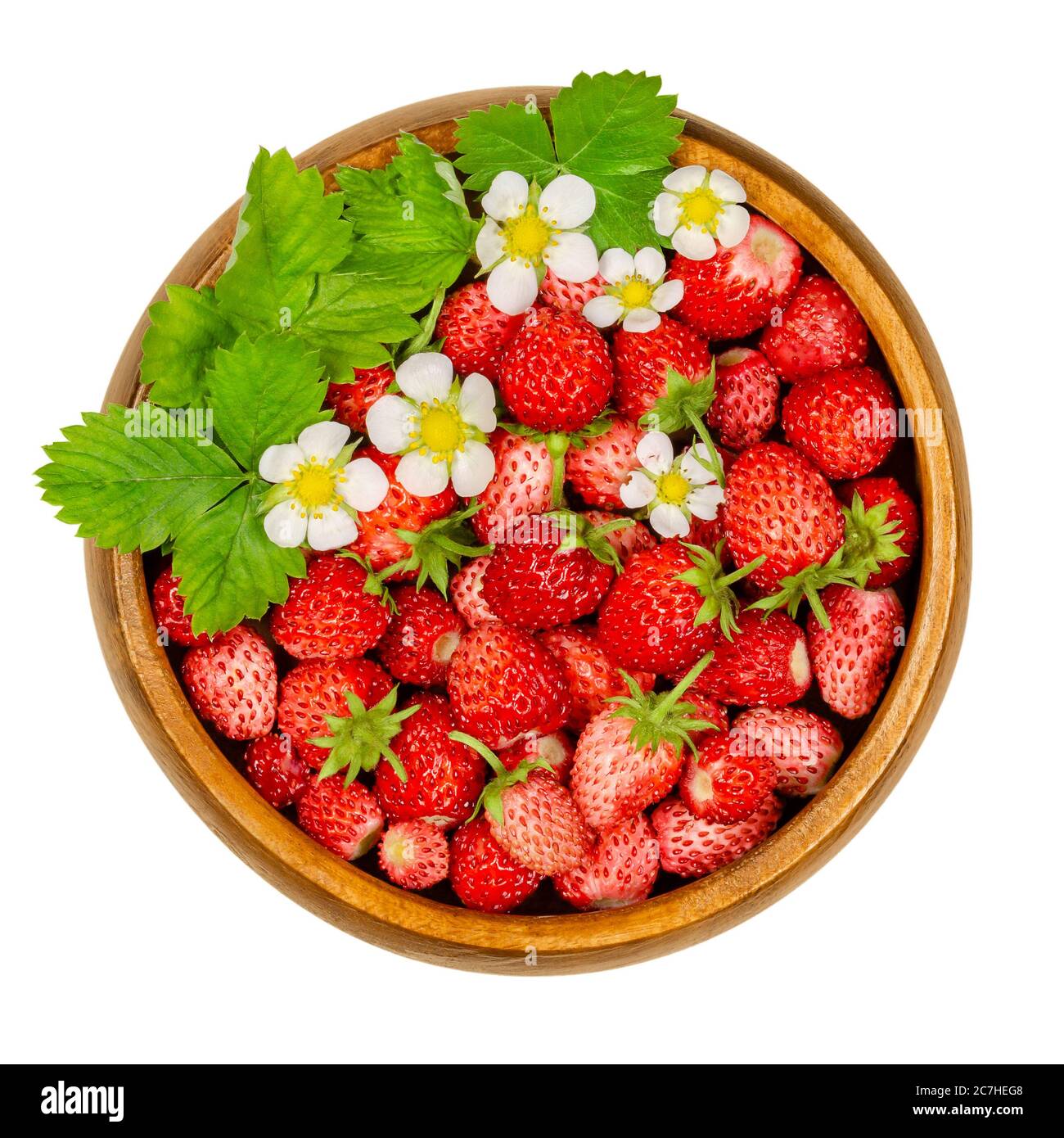 Wild strawberries in wooden bowl. Small ripe Alpine strawberries, also woodland, Carpathian or European strawberry, with leaves and flowers. Stock Photo
