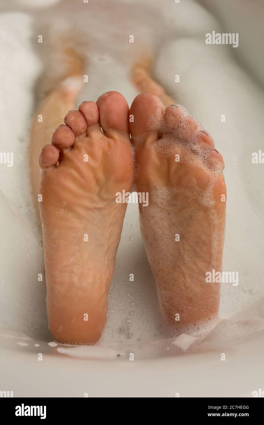 Soles of two wet feet poking out of bubble bath in tub. Unidentified young caucasisan woman Stock Photo