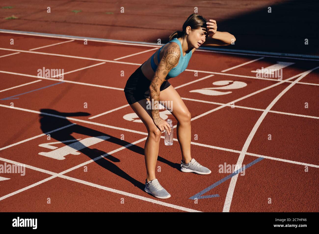 Young athlete woman in sportswear with bottle of water tiredly leaning