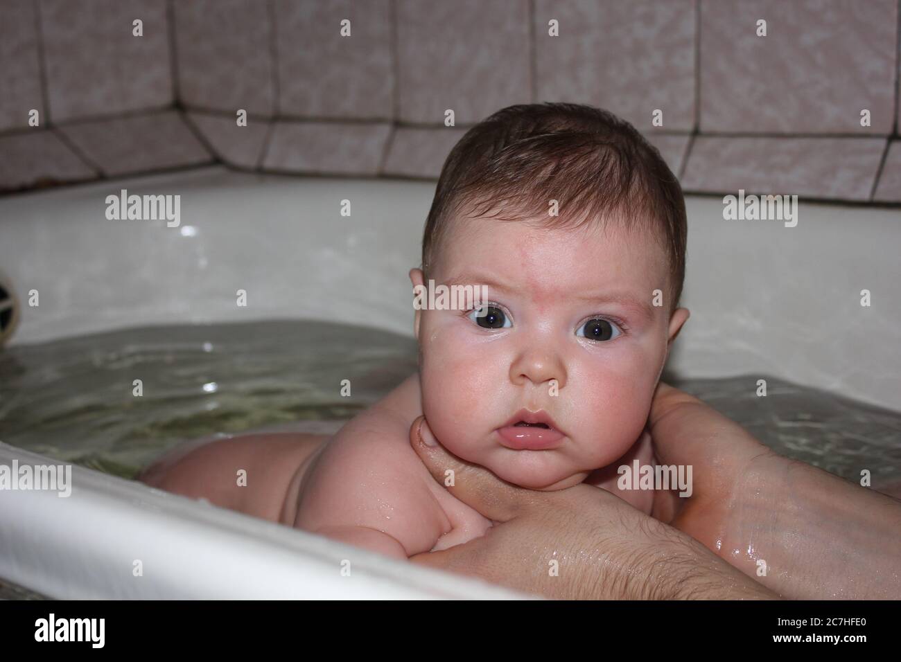 Bathing baby in a large bath. A child boy younger than six months swims