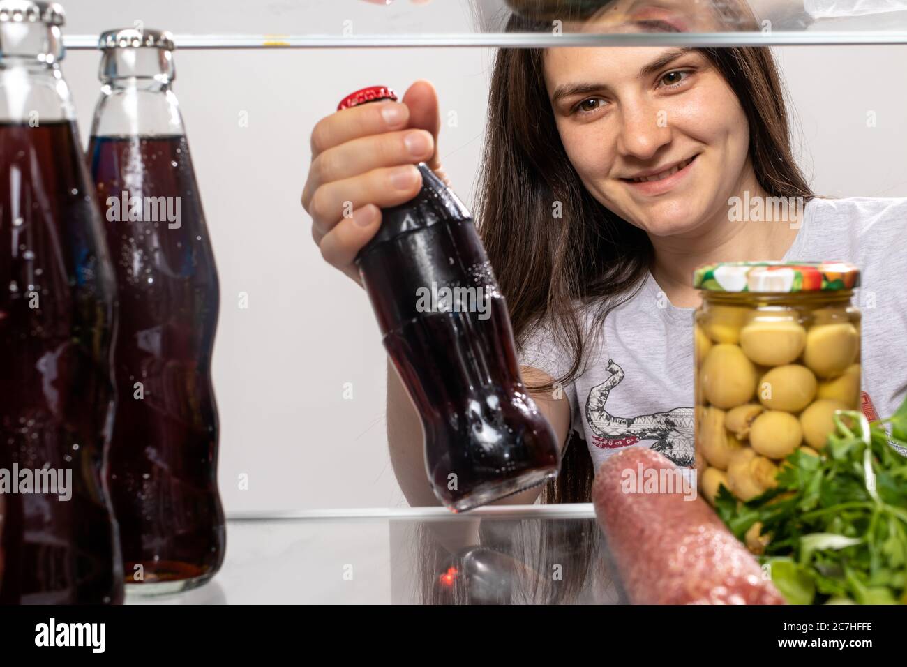 The girl looks in the fridge and takes out fruit juice in a glass