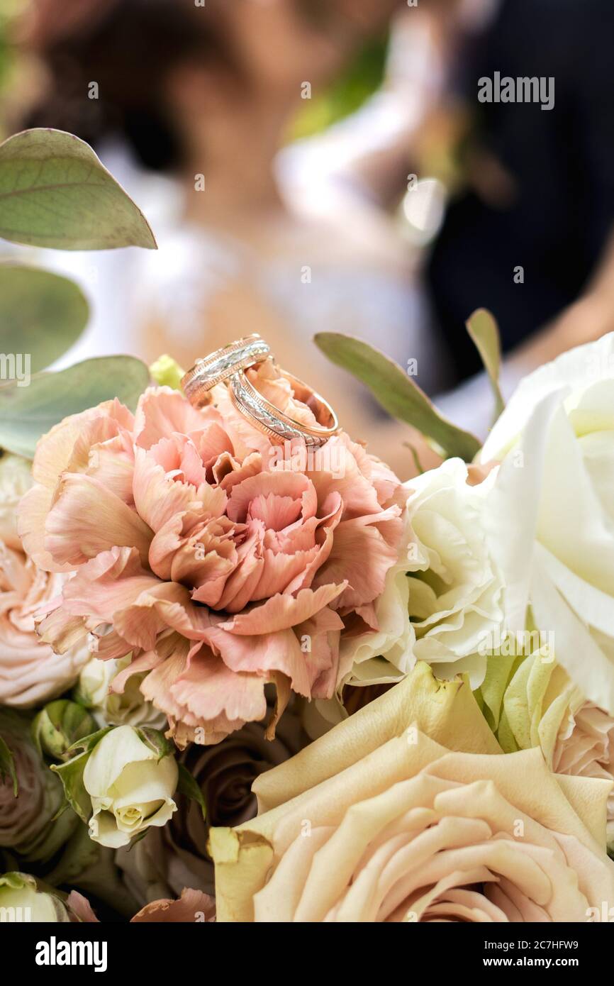 Gold wedding rings on a bride's bouquet of pink, yellow and white delicate roses. Stock Photo