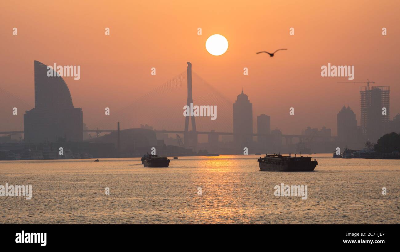 Sun rising above Huangpu River. Colorful dusk with Yangpu Bridge in the background. Stock Photo