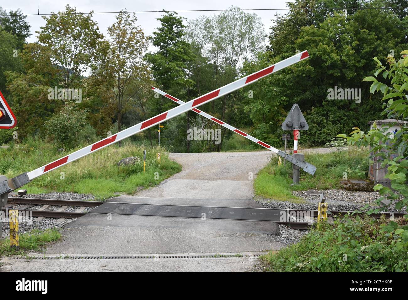 Railway crossing with a opening barrier or gates and signalling in the spot where country road crossing railroad near the forest. Stock Photo