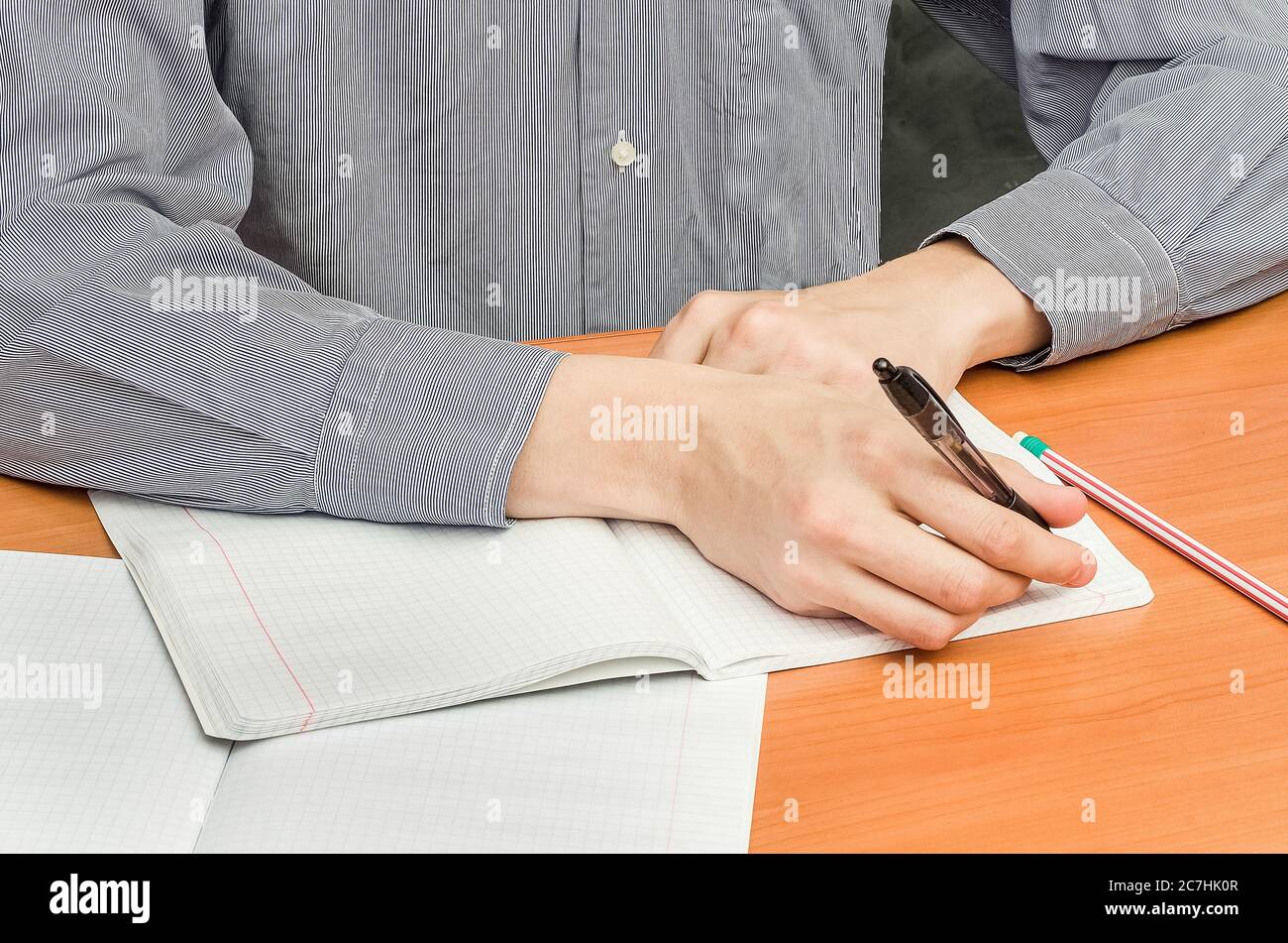 A student in a shirt sits at a table and writes an abstract. School lessons, classes at the university. Stock Photo