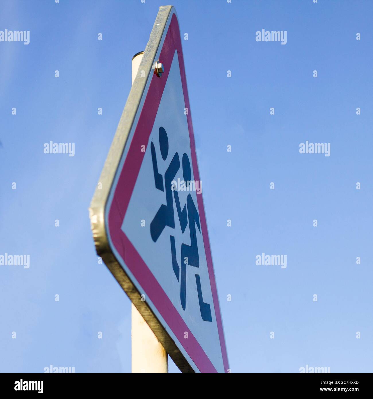 Information road sign, triangular white shield with running figures on blue sky background. Attention, school ahead, reduce speed recommendation. Stock Photo