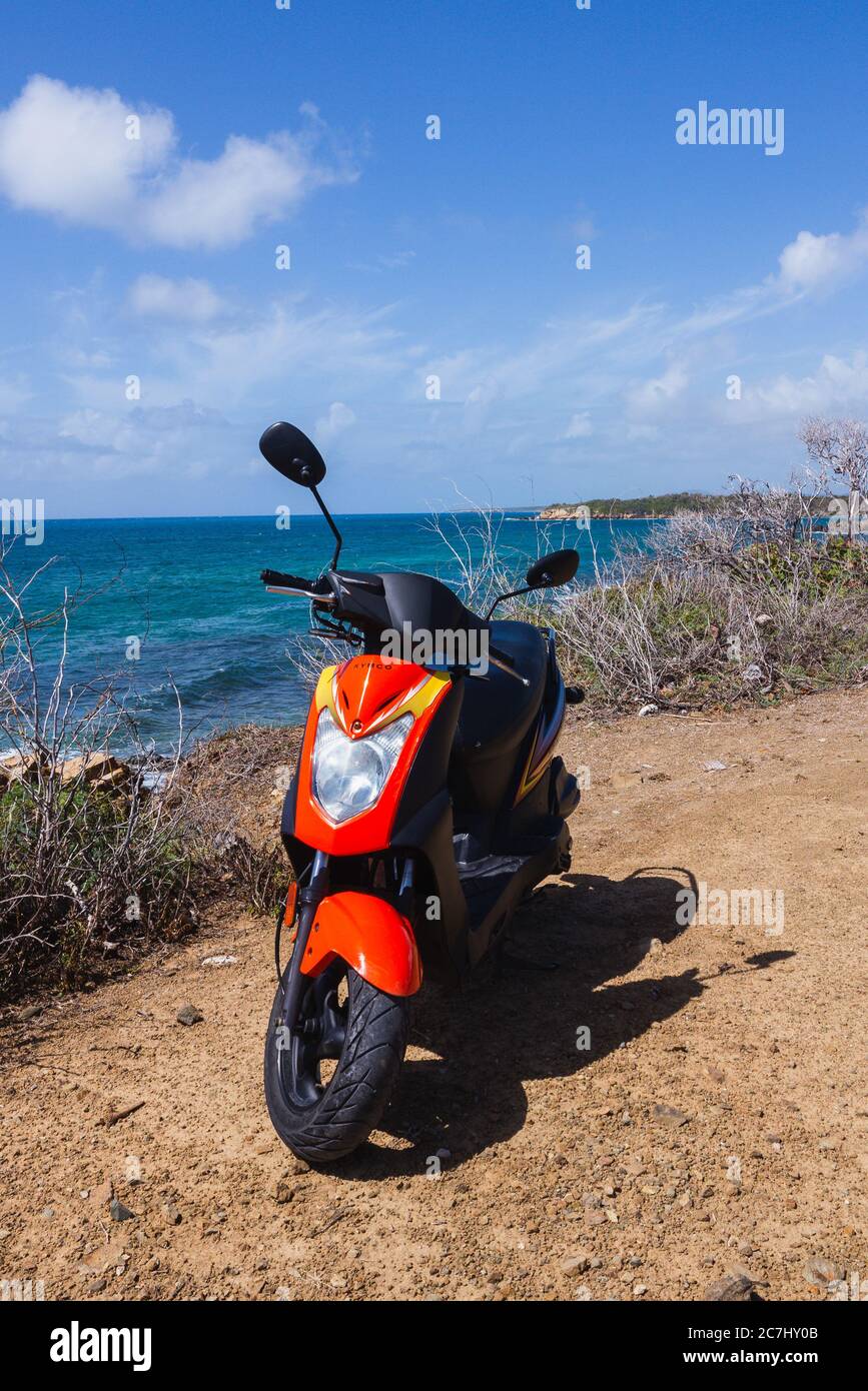 A red scooter on a sandy viewpoint overlooking the Caribbean Sea in