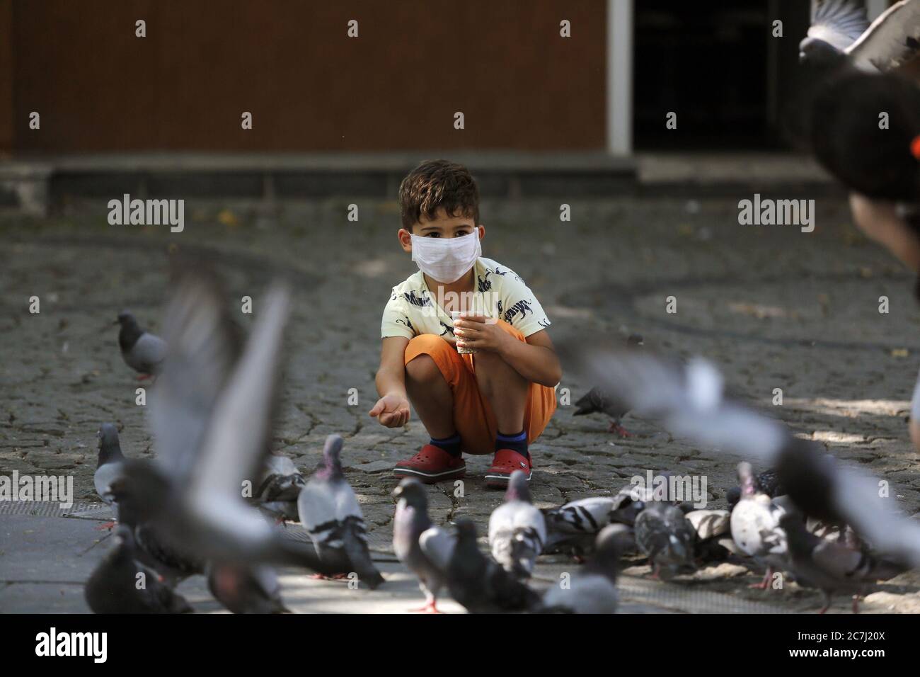 Ankara, Turkey. 17th July, 2020. A boy wearing a face mask feeds pigeons at a park in Ankara, Turkey, on July 17, 2020. Turkish Health Minister Fahrettin Koca on Friday warned of the increasing number of intensive care and intubated COVID-19 patients in the country. Turkey's daily coronavirus cases increased by 926 on Friday, raising the overall number to 217,799, the minister said. Credit: Mustafa Kaya/Xinhua/Alamy Live News Stock Photo