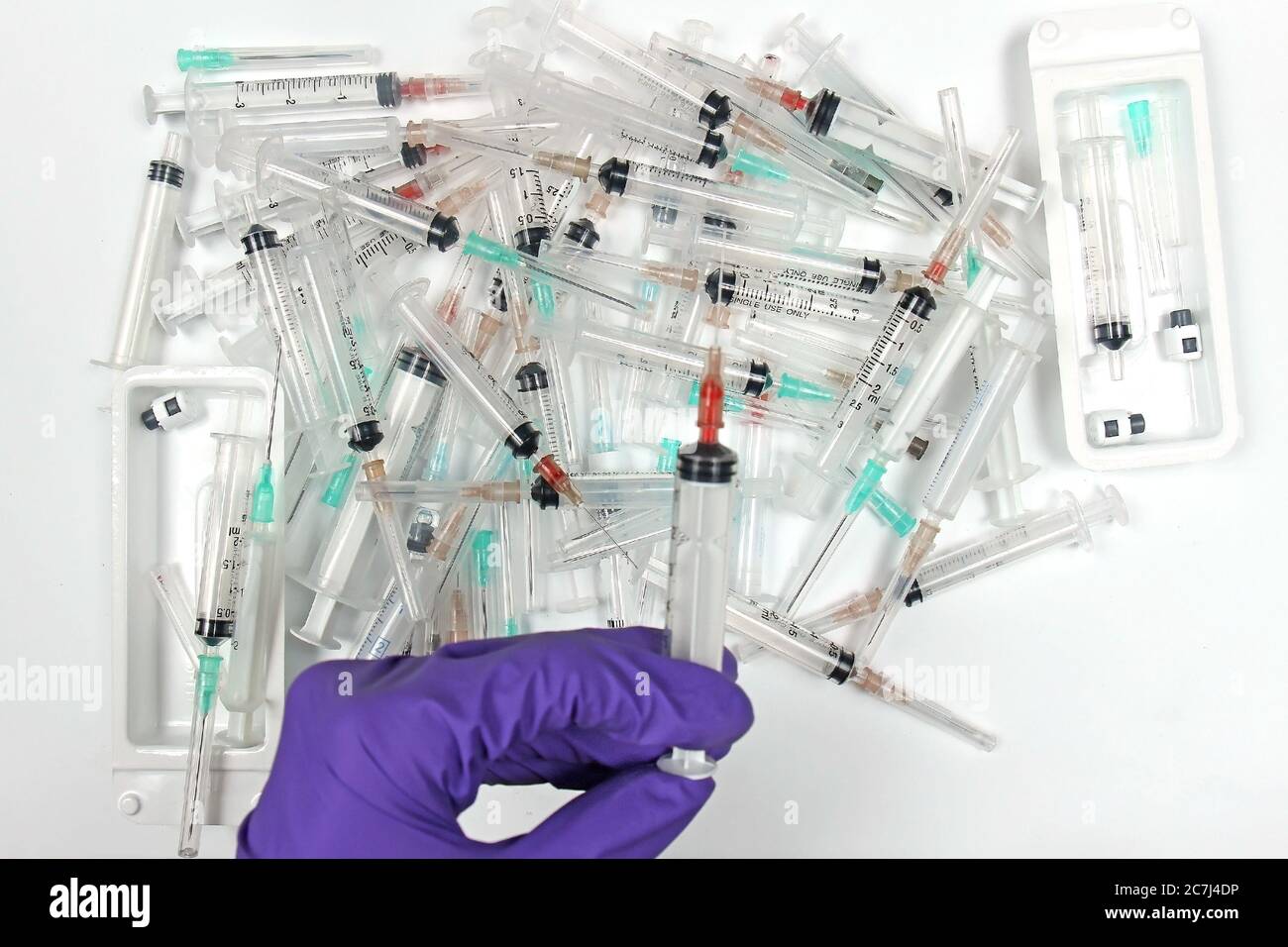 Medical person hand in glove over large pile of used syringes and needles Stock Photo