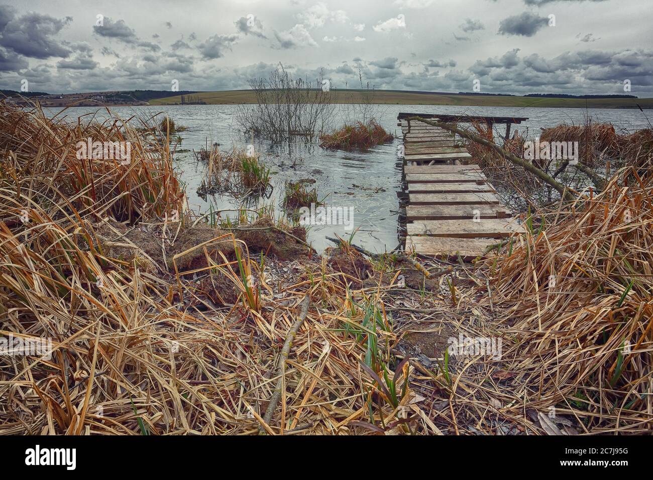 Old wooden pier with dry reed. Cloudy weather Stock Photo
