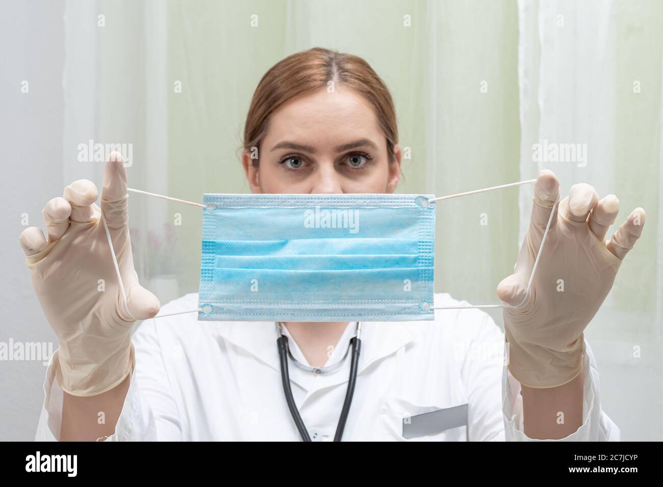 female doctor putting medical mask on her face in doctors office Stock