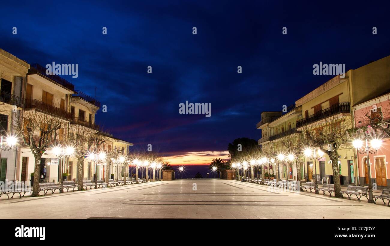 Etna, Etna National Park, Parco dell –´Etna, Zafferana Etnea, dawn, night blue sky, Piazza Umberto I Belvedere, empty square, sunrise in the background, buildings and street lamps to the right and left of the square Stock Photo